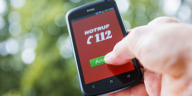 Hand tippt auf grünen Anrufbutton mit der Notrufnmmer 112 auf Smartphone