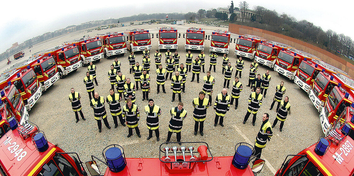 Feuerwehrleute in Schutzkleidung stehen in einem großen Kreis von Feuerwehrfahrzeugen auf der Theresienwiese