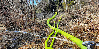 Leuchtend gelbe Schläuche der Feuerwehr verlaufen über trockenes Gras und Zweige in einem Waldgebiet