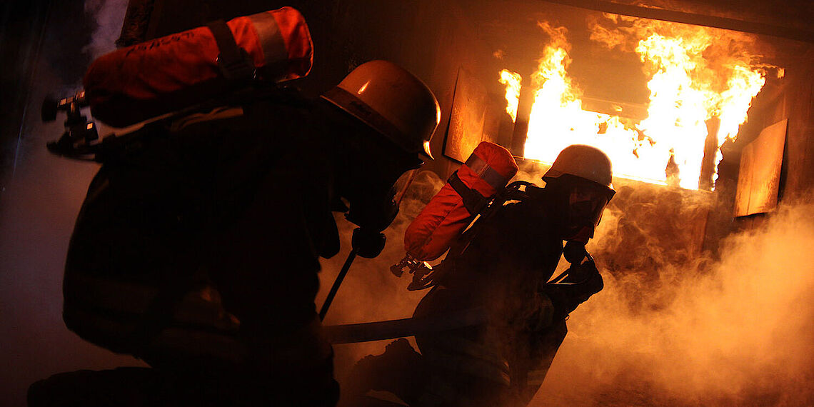 Zwei Feuerwehrleute unter Atemschutz bei einer Brandübung mit Flammen und Rauch Zwei Feuerwehrleute unter Atemschutz bei einer Brandübung mit Flammen und Rauch
